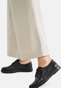 Pantofi negri din piele, cu sireturi, cu vârf rotund, suprafață texturată și talpă din cauciuc, asortați cu pantaloni crem cu picior larg.