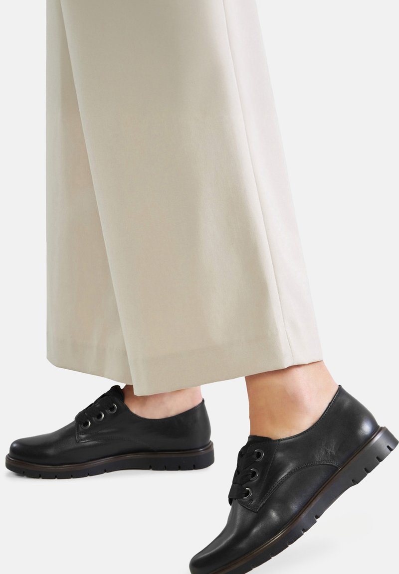 Pantofi negri din piele, cu sireturi, cu vârf rotund, suprafață texturată și talpă din cauciuc, asortați cu pantaloni crem cu picior larg.