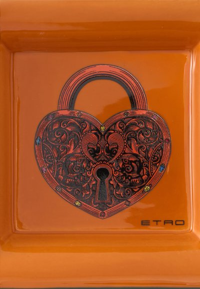 Cadenas ornemental en forme de cœur avec des motifs noirs et rouges complexes et des détails de pierres précieuses colorées, posé sur un plateau carré orange avec le logo ETRO.