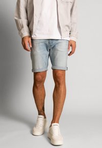 Shorts din denim de culoare albastru deschis, cu mansete răsucite, asortați cu un tricou alb și o jachetă gri deschis, completat de adidași bej.