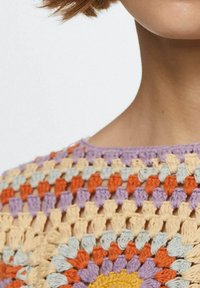 Top de ganchillo con un patrón multicolor que incluye hilos en naranja, púrpura, amarillo y azul claro; diseño de calado y acabado texturizado.