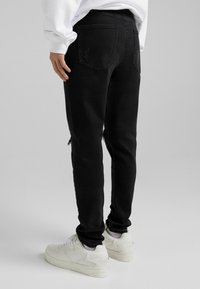 Svarta denimjeans med slim fit, med en sliten detalj på knäet, två bakfickor, kombinerat med vita sneakers.