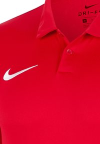 Polo rosso realizzato in tessuto traspirante, con colletto a punta, due bottoni e logo Nike bianco a forma di swoosh sul lato sinistro del petto.