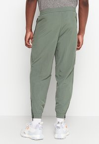 Lekki, oliwkowozielony dres z elastycznym pasem, bocznymi kieszeniami na zamek i zwężanymi mankietami, wykonany z gładkiego, oddychającego materiału.