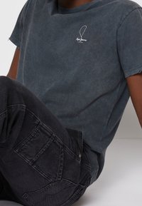 Šedé vybledlé tričko s kulatým výstřihem, vyšívaným logem na hrudi, spárované s černými texturovanými cargo kalhotami s několika kapsami.