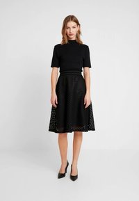 Črna obleka z oprijetim zgornjim delom s kratkimi rokavi in razširjeno krilom. Krilo ima teksturo z diagonalnimi črtami in izrezanimi vzorci.