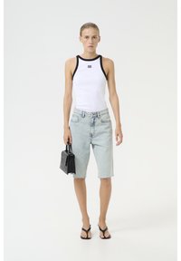 Vit ribbad tanktopp med svart kant, ljusblå denimbermuda-shorts, handväska i svart krokodilpråm och svarta sandaletter med remmar.