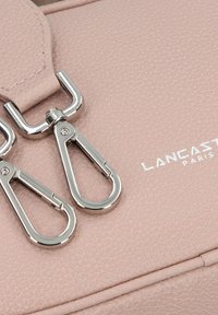 Superficie in pelle rosa testurizzata con chiusure e dettagli di cucitura in metallo argento. Presenta il marchio embossato "Lancaster Paris".
