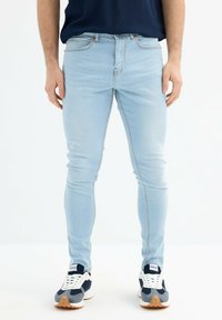 Jeans ajustados de color azul claro con un ligero desgaste, diseño de cinco bolsillos, costuras en contraste, combinados con zapatillas azul marino y blancas.