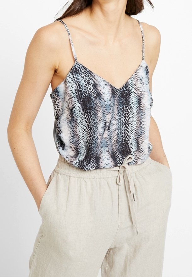 Kvinna iförd en ärmlös topp med ormskinnsmönster och tunna band, instoppad i beiga linnebyxor med dragsko, med händerna i fickorna.