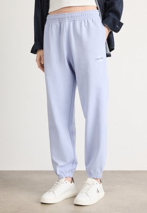 Lyslilla joggingbukser med elastisk talje og manchetter. Har et lille hvidt logo på benet. Parret med hvide sneakers.