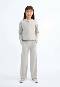 Sivasti pleten kardigan z gumbi in ujemajoče se ohlapne hlače. Gladka tekstura, sproščen dizajn, v kombinaciji z srebrnimi ravnimi čevlji. Enostavna ozadje.