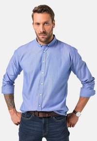 Lichtblauwe overhemden met kraag, lange mouwen en een slim fit, gecombineerd met donkere jeans en een bruine riem. Subtiele logo-detail.