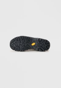 Black rubber sole with deep treads for traction, featuring a central yellow logo and textured surface for enhanced grip.