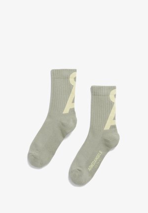 Calze in cotone misto verde chiaro con texture a coste, dotate di un logo giallo prominente su ciascun lato e una punta rinforzata.