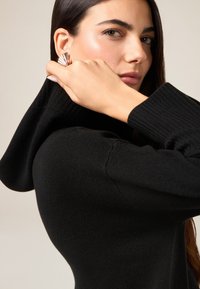 Czarny prążkowany sweter z wysokim kołnierzem o miękkiej fakturze. Błyszcząca metaliczna kolczyk z motywem wachlarza i ozdobami z kamieni.