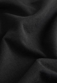 Primo piano della trama di un tessuto nero con modello a maglia visibile e morbide pieghe che creano ombre.