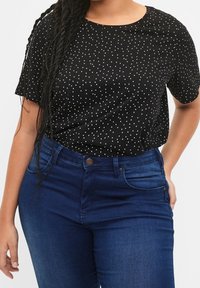 Schwarzes Kurzarm-T-Shirt mit weißen Punkten, rundem Ausschnitt, kombiniert mit dunkelblauen hoch taillierten Jeans mit Knopfverschluss.