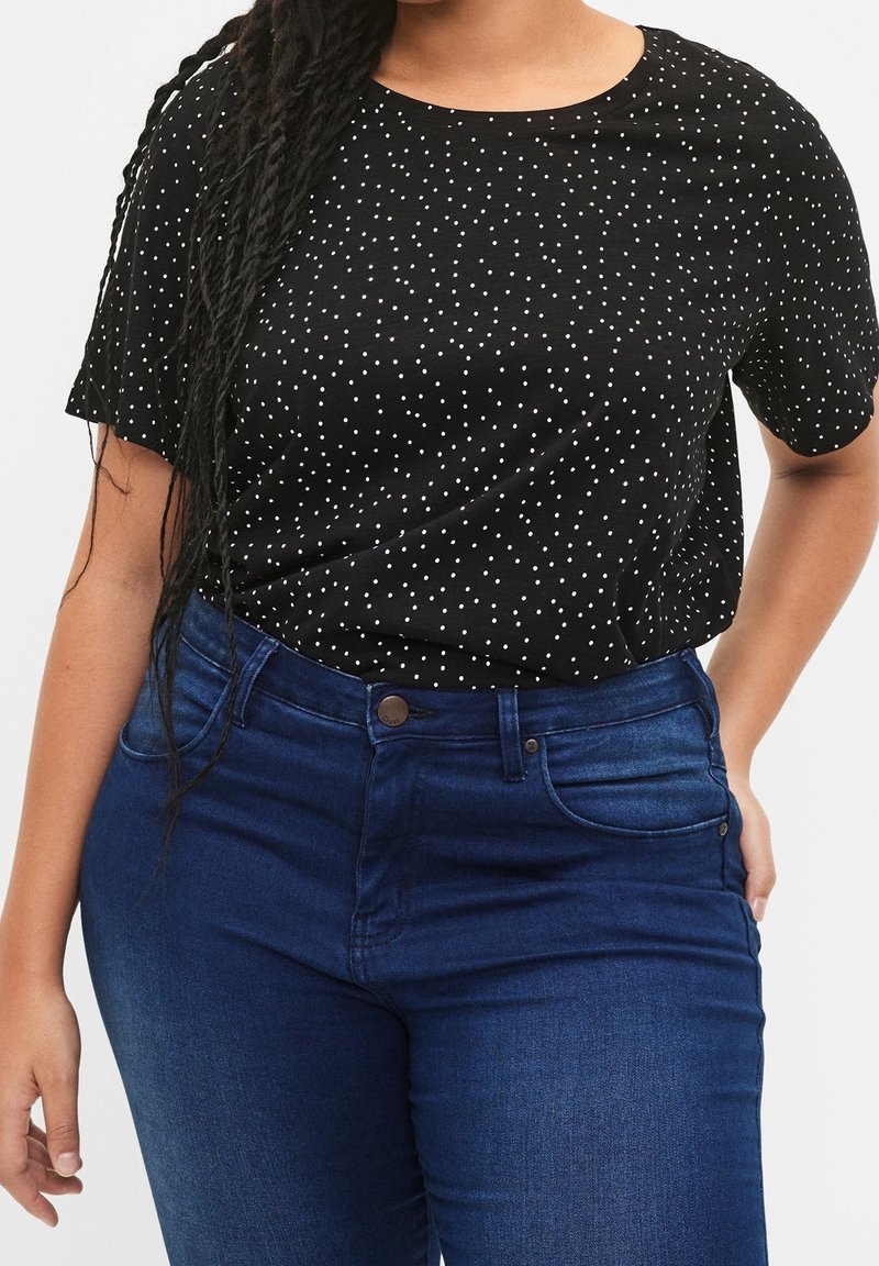 Schwarzes Kurzarm-T-Shirt mit weißen Punkten, rundem Ausschnitt, kombiniert mit dunkelblauen hoch taillierten Jeans mit Knopfverschluss.
