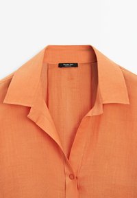 Korte mouw overhemd in lichtoranje stof met een klassieke kraag en knoopsluiting. Bevat een subtiele textuur en een label met de tekst "Massimo Dutti."