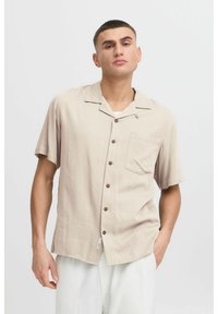 Korte mouwen beige overhemd van lichtgewicht stof, met een knoopsluiting aan de voorkant, een borstzak en bruine knopen. Glad textuur en relaxte pasvorm.
