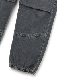 Grijze denim broekspijpen met elastische boorden en een gestikte flapdetail nabij de knie, weergegeven op een witte achtergrond.