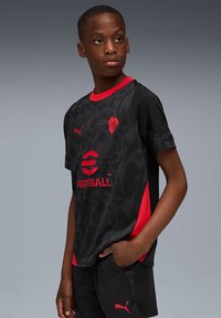 Melns un sarkans futbols krekls ar īsām piedurknēm, ar rakstainu dizainu, apaļu izgriezumu un logo akcentiem. Materiāls izskatās viegls.