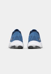 Baskets de sport bleues en mesh respirant avec une surface texturée, semelle intermédiaire blanche et semelle extérieure grise. Logo notable sur le côté.