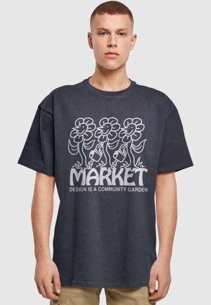 Dark gray oversized t-shirt featuring a graphic of flowers and the text "MARKET DESIGN IS A COMMUNITY GARDEN" in white. Cotton fabric.