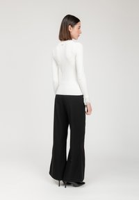 Witte lange mouwen top met kantaccenten bij de manchetten, gecombineerd met zwarte wijde broek, gezien vanaf de achterkant. Eenvoudig ontwerp, gestructureerde stof.