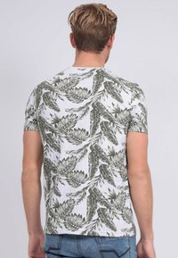 T-shirt à manches courtes avec une base blanche et un motif de feuilles vertes, fabriqué dans un tissu léger et avec une coupe décontractée.
