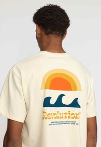 Katoenen T-shirt in crème met een kleurrafische afbeelding van een zon en golven op de achterkant. Heeft gedurfde oranje, gele, blauwe en groene tinten.