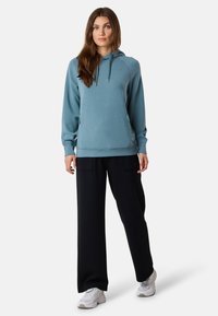 Blauw sweatshirt met capuchon, lange mouwen en zijzakken, gecombineerd met zwarte wijde broek en lichtgekleurde sneakers.