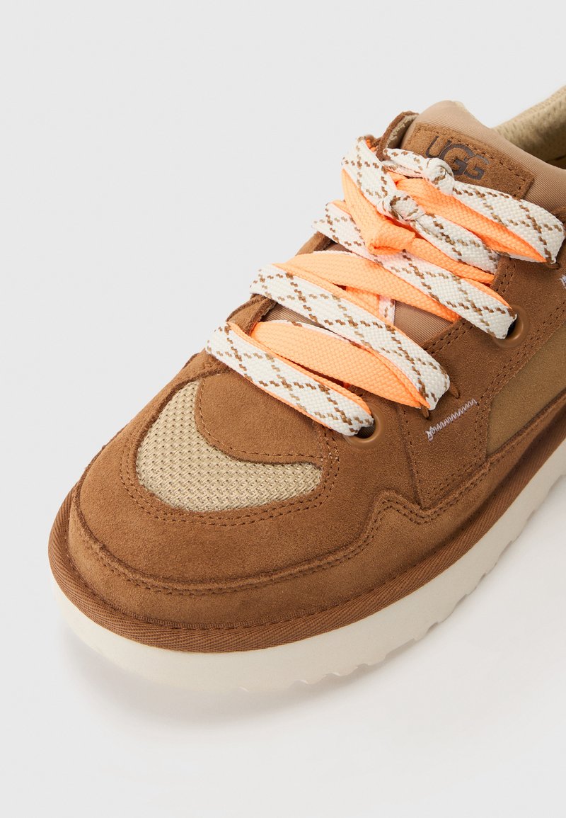 Braune Sneaker mit einem Obermaterial aus Wildleder und Mesh, strukturierten Akzenten und flachen Schnürsenkeln mit orangenen Highlights. Dicke weiße Gummisohle.