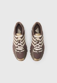 Ténis desportivos castanhos e bege com parte superior em malha, três riscas, biqueira redonda e atacadores planos. Apresentam sola de borracha texturada.