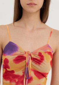Flerfarget halterneck-top i lett stoff med oransje, lilla og røde tie-dye mønstre; har justerbare stropper og en rynkedetalj.