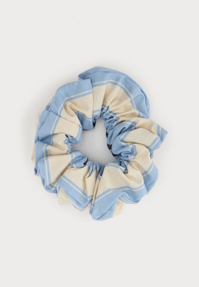 Μπλε και κρεμ υφασμάτινο scrunchie με τετράγωνο σχέδιο, συγκεντρωμένο σε κυκλικό σχήμα σε ανοιχτό φόντο.