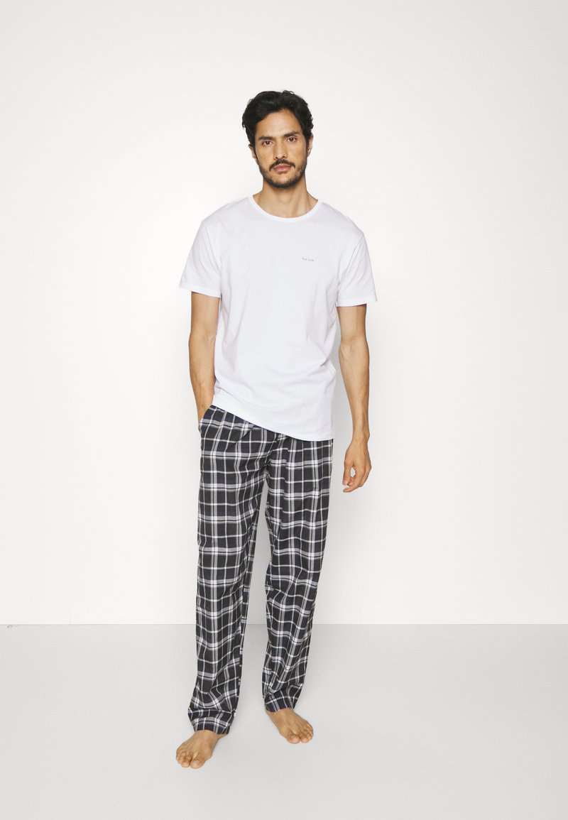 Camiseta blanca de manga corta con una marca sutil, combinada con pantalones de pijama de cuadros en blanco y negro. Tela de algodón, ajuste relajado, sin calzado.