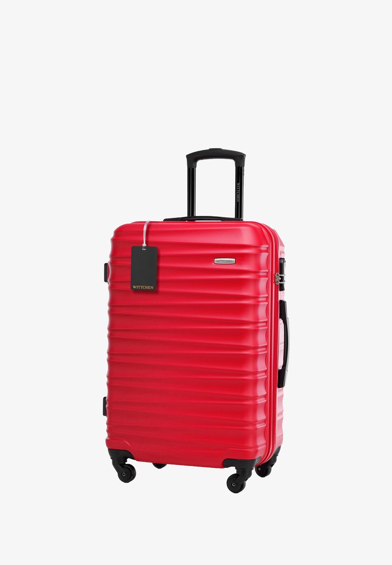 Červený tvrdý kufr s drážkovaným designem, teleskopickou rukojetí a černými kolečky. Obsahuje štítek na zavazadla připevněný k zipu.