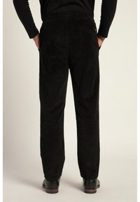 Schwarze Cord-Hosen mit strukturiertem Finish, elastischem Bund und Rückentaschendetail, kombiniert mit schwarzen Schuhen.