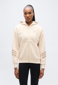 Μπεζ φούτερ με φερμουάρ και κουκούλα, κατασκευασμένο από απαλό ύφασμα. Διαθέτει διακριτικό σχέδιο με τρεις ρίγες στα μανίκια και μικρό λογότυπο στο στήθος.