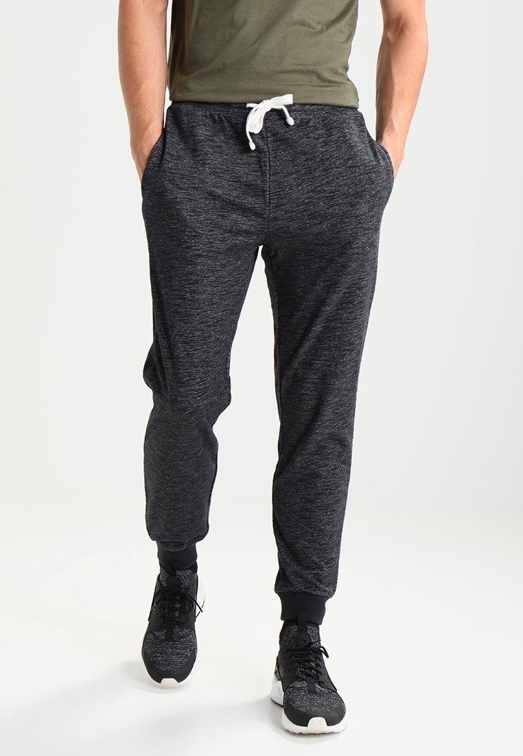 Men's black jogger pants with a textured finish, elastic waistband, white drawstring, and tapered legs, paired with black athletic shoes.