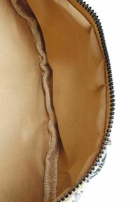 Beiger Innenfutter einer Tasche mit einer strukturierten, welligen Naht und schwarzem Reißverschlussdetail entlang des Randes. Keine äußeren Muster sichtbar.