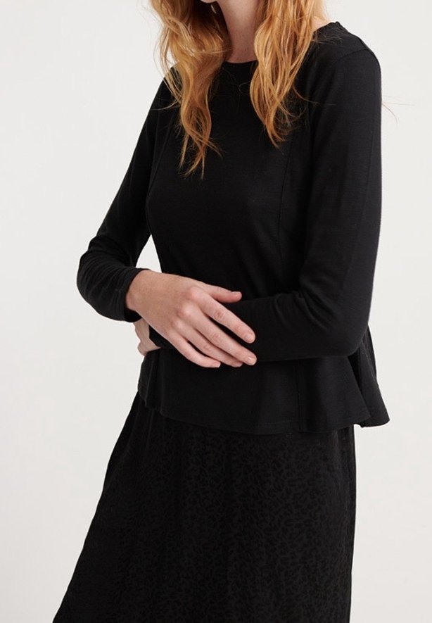 Musta pitkähihaisvaate, joka on valmistettu pehmeästä kankaasta; siinä on liehukassa ja pyöreä pääntie, yhdistetty mustan hameen kanssa, jossa on hienovaraista pintarakennetta.