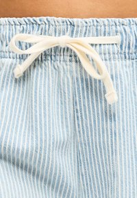 Κοντινό πλάνο από μπλε και λευκό παντελόνι με κάθετες ρίγες και λευκό κορδόνι δεμένο σε φιόγκο στη ελαστική μέση.