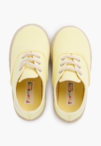 Baskets en toile jaunes avec bouts ronds, lacets beiges et semelles en caoutchouc texturé. L'intérieur comporte une étiquette colorée avec "Pisamonas."