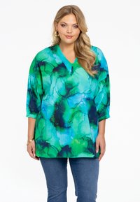 Groene en blauwe V-hals tuniek met abstracte aquarelpatronen, losse pasvorm, driekwartmouwen, gestructureerde stof, gecombineerd met jeans.