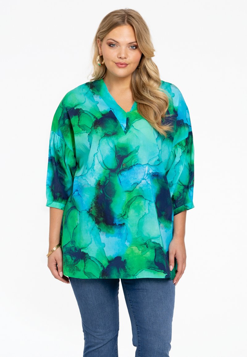 Groene en blauwe V-hals tuniek met abstracte aquarelpatronen, losse pasvorm, driekwartmouwen, gestructureerde stof, gecombineerd met jeans.