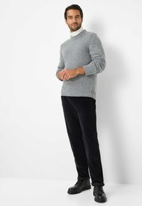Grijze gebreide coltrui met geribbelde manchetten en onderrand, gecombineerd met zwarte corduroy broek en zwarte veterboots. Eenvoudig ontwerp, neutraal palet.