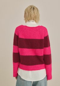 Pletený sveter s horizontálnymi pruhmi v jasne ružovej a tmavej burgundskej farbe, s mäkkou štruktúrou a mierne skráteným strihom.